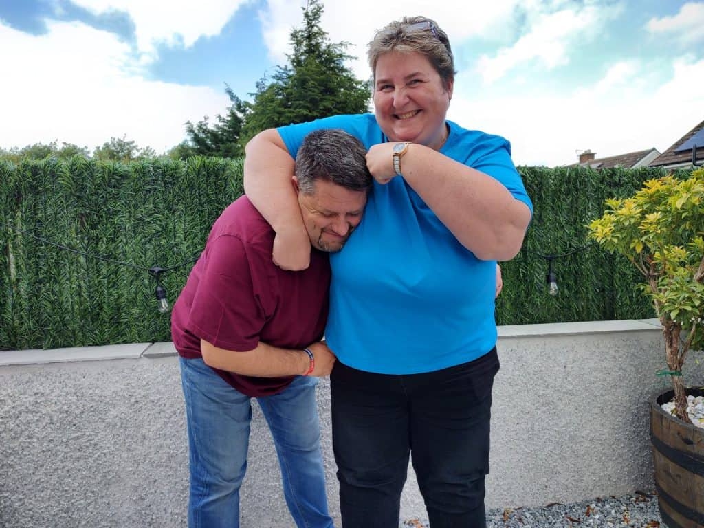 Brenda and Steve McKenzie hugging each other in front of a house.