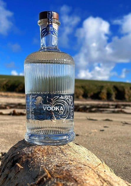 A bottle of Orkney Vodka sits on a rock beach.
